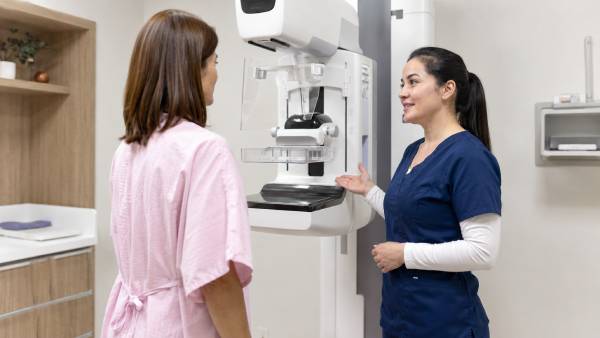 pacijentkinja razgovara sa medicinskom sestrom pored mamografa tokom dijagnostike raka dojke